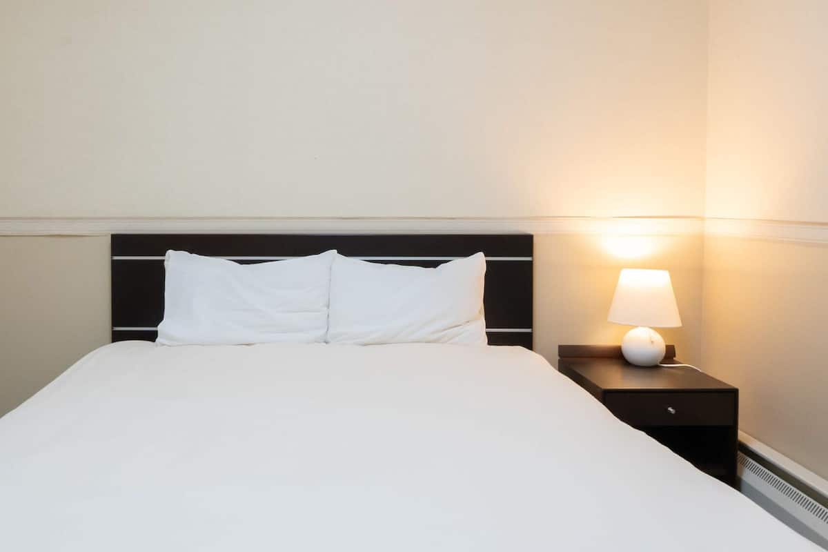 A neatly made bed with white linens, a black headboard, and a bedside lamp on a nightstand.