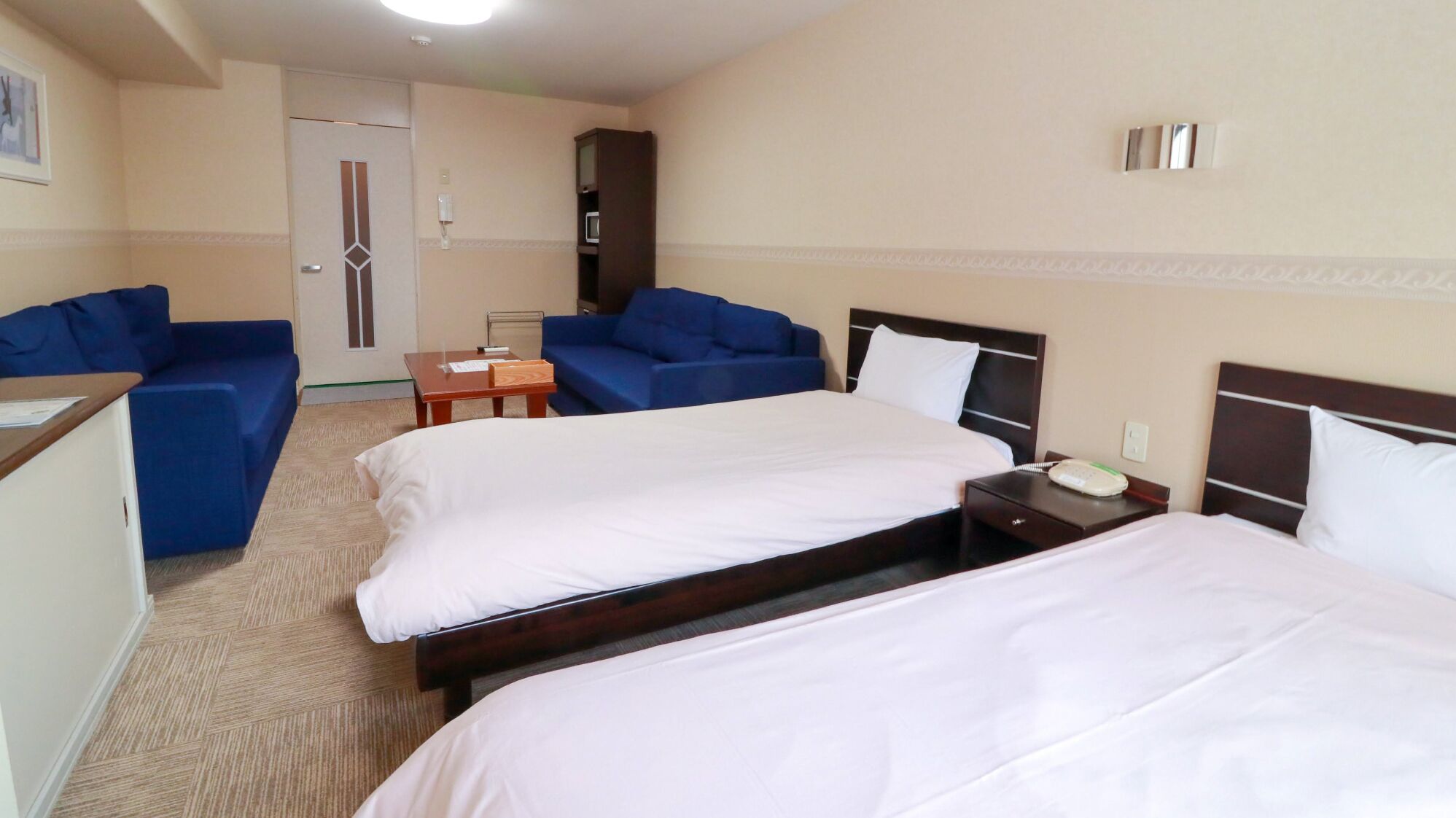 A hotel room with two beds, a desk, a chair, and a blue sofa.