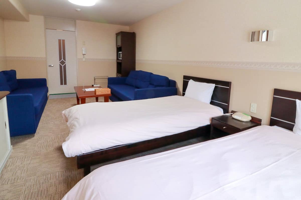 A hotel room with two beds, a desk, a chair, and a blue sofa.