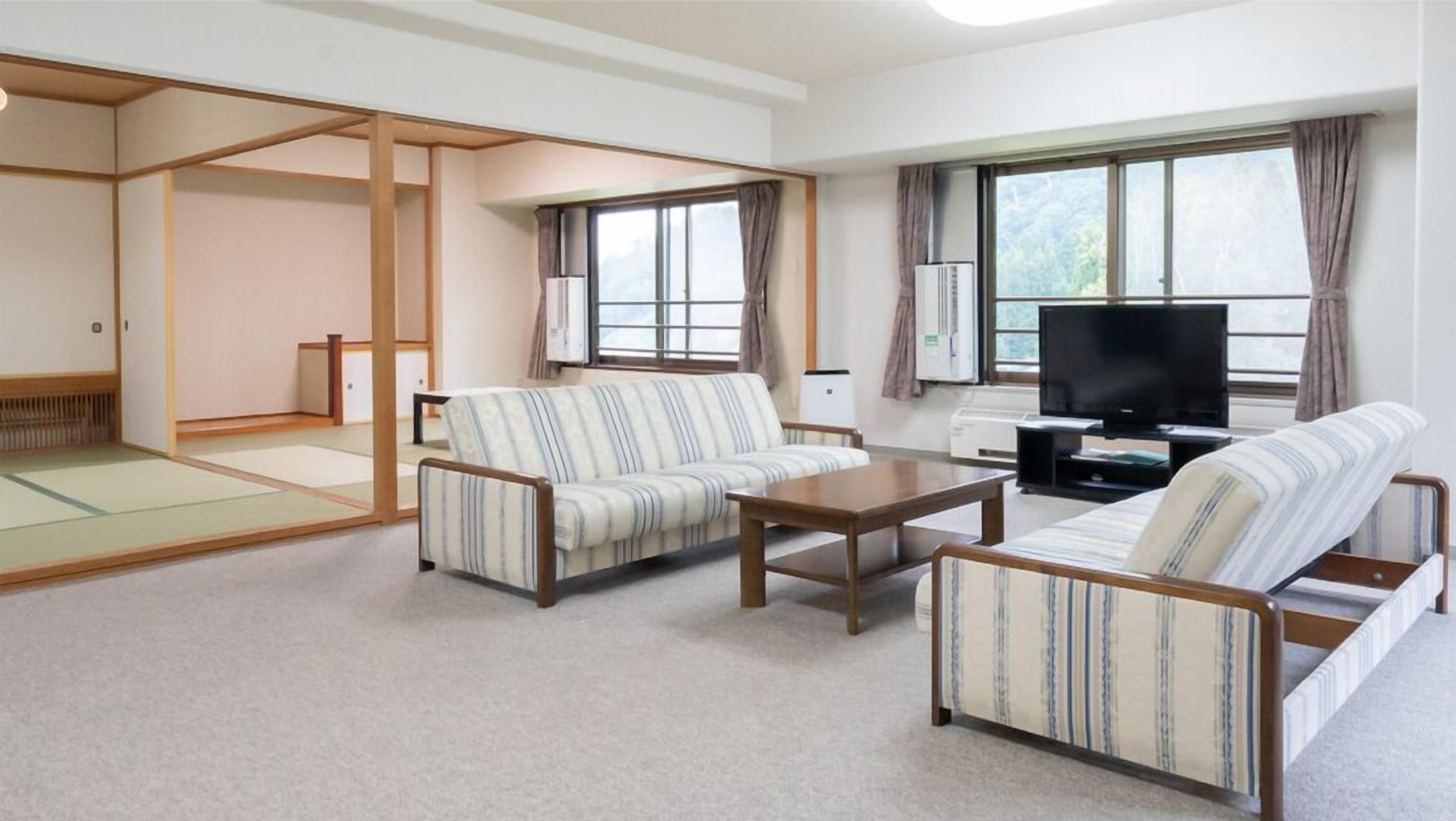 Un salon de style japonais traditionnel, avec des tatamis, un canapé, une table basse et un téléviseur.