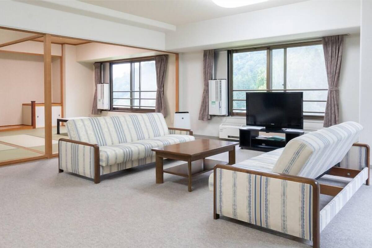 A traditional Japanese-style living room with tatami mats, a sofa, a coffee table, and a television.