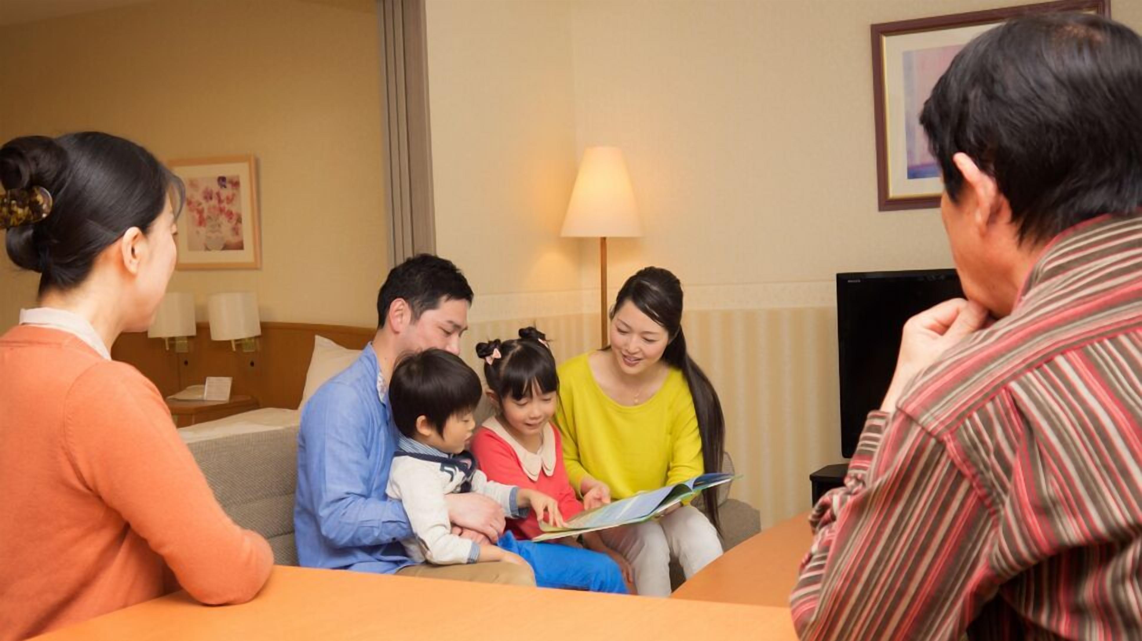 A family of four in a hotel room with a sofa, a table, and a lamp.