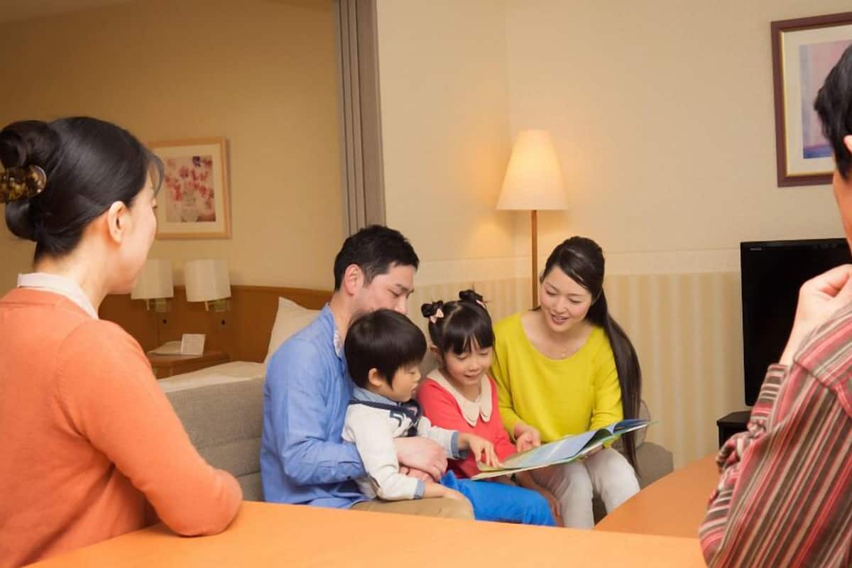 A family of four in a hotel room with a sofa, a table, and a lamp.