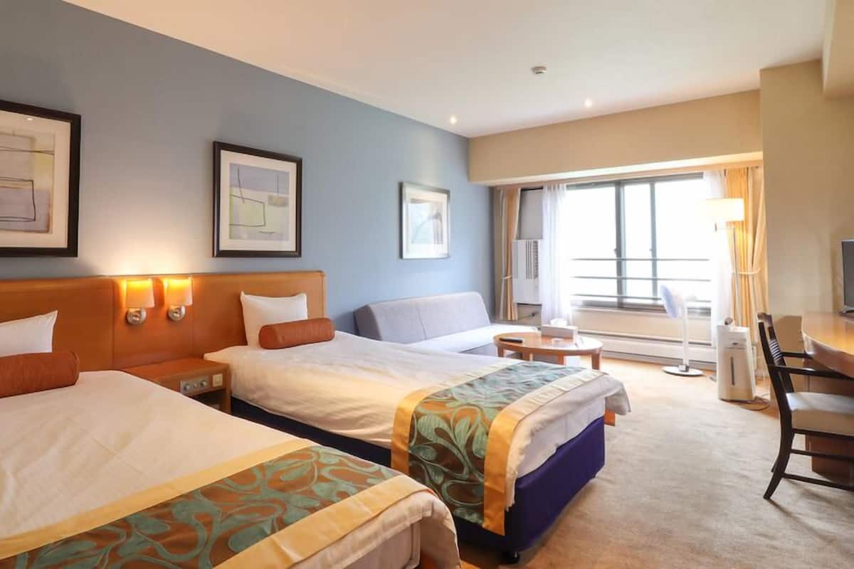 A hotel room with two beds, a desk, a chair, and a large window.