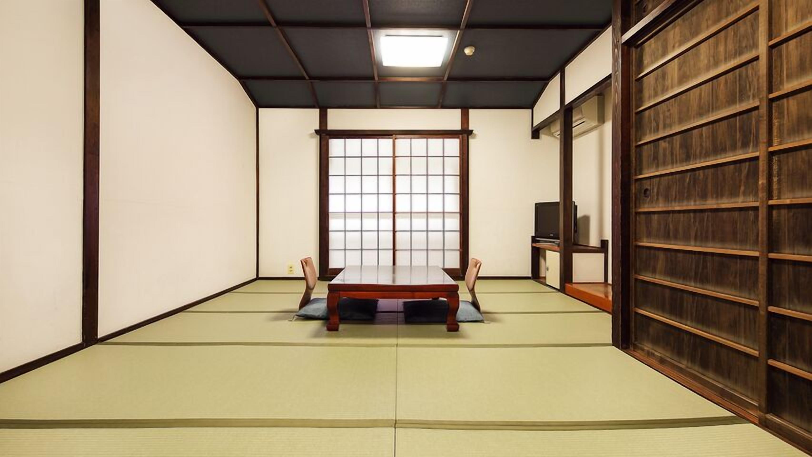 Una habitación con tatami, una mesa baja, sillas, una puerta corredera y un televisor sobre un soporte de madera.