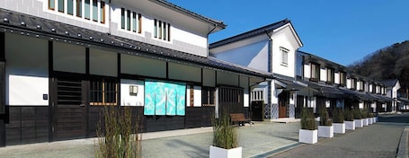 A row of traditional-style buildings with a covered walkway, potted plants, and a bench.