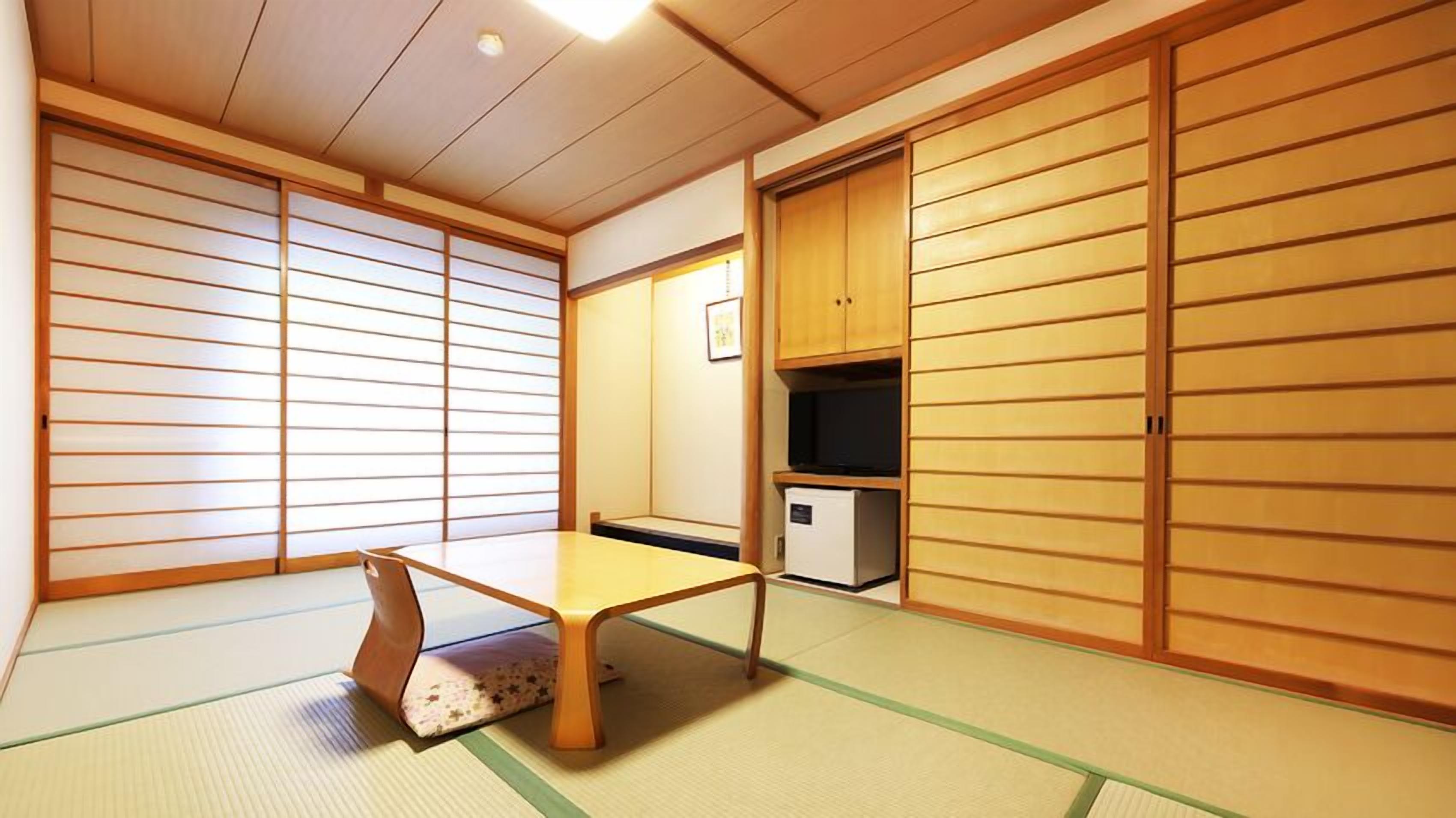 Una habitación japonesa tradicional con suelo de tatami, una mesa baja, puertas correderas y un televisor.