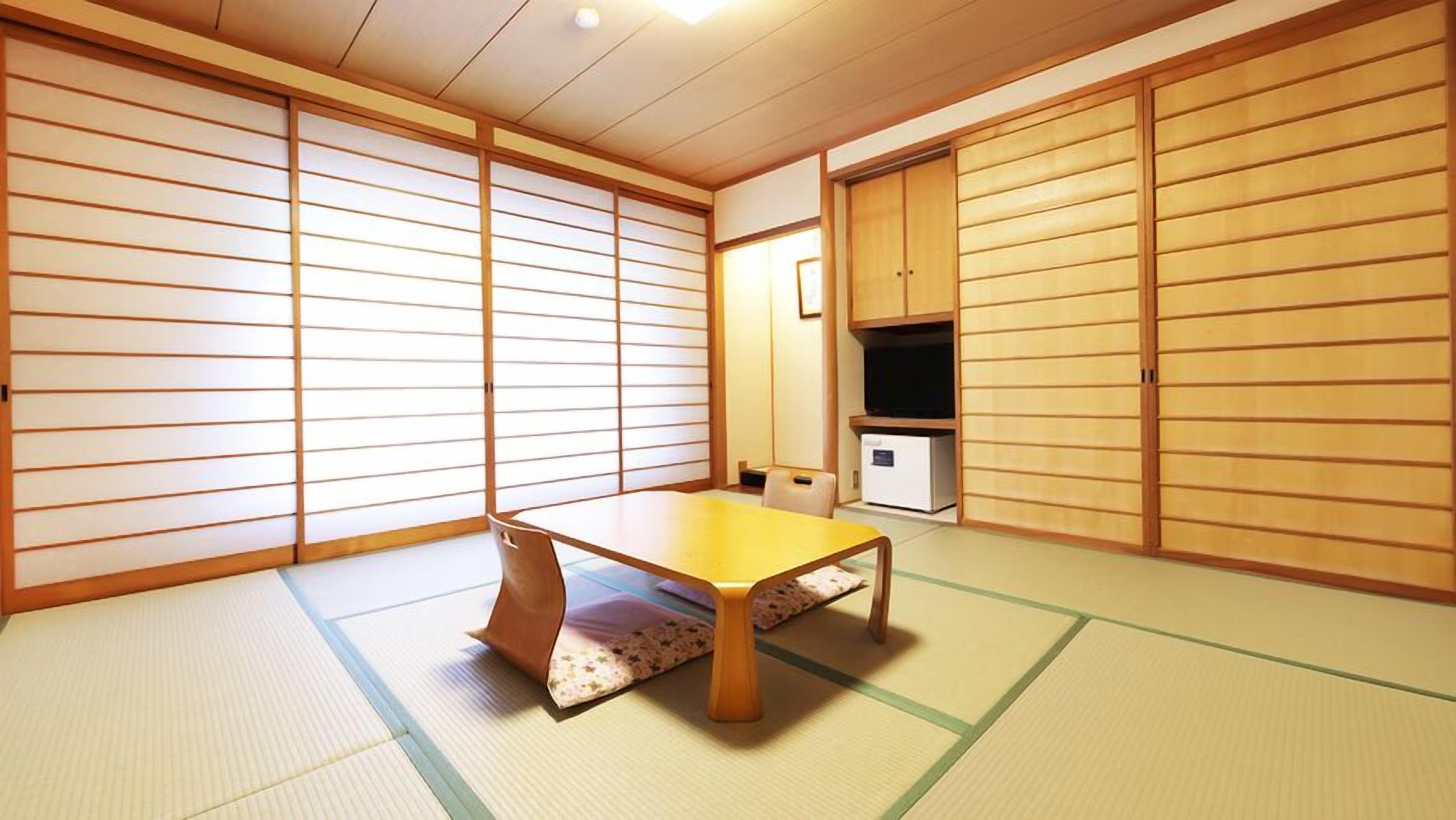 Una habitación japonesa tradicional con suelo de tatami, una mesa baja, puertas correderas y un mueble empotrado para la televisión.