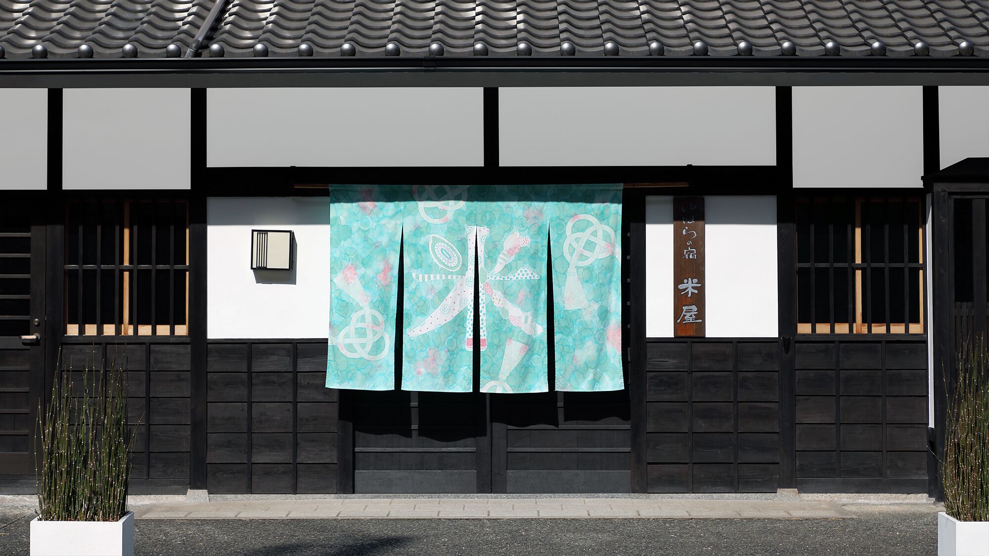 A traditional Japanese building with a tiled roof, black wooden walls, and a green patterned curtain.