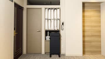 A hotel room with a closed door, a wardrobe with hanging robes, a suitcase, and a wall-mounted phone.