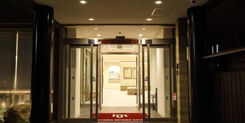 La entrada del HOTEL FUYAMA MIYAKO, con un escaparate de vidrio y una alfombra roja que conduce al interior.
