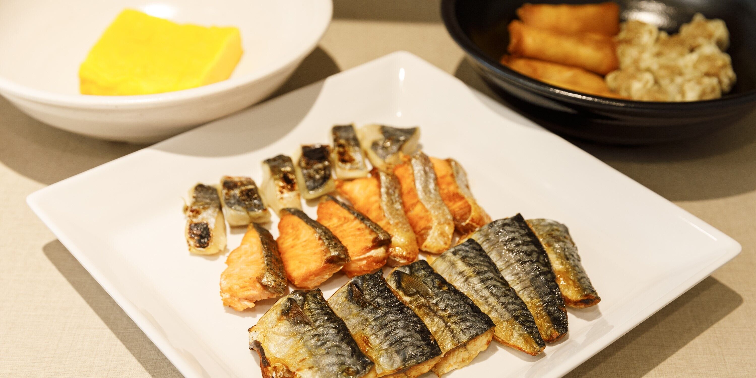 A plate of grilled fish with a bowl of butter and a bowl of fried items in the background.
