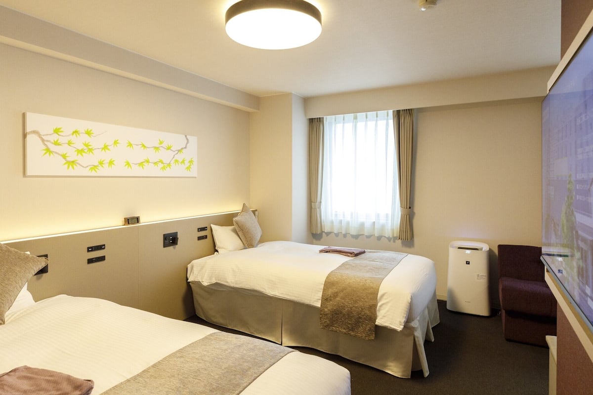 Ein Hotelzimmer mit zwei Betten, einem Flachbildfernseher, einem Fenster mit Vorhängen und einem Wandbild.