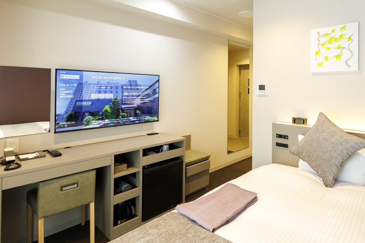 Ein Hotelzimmer mit einem Bett, einem Schreibtisch mit Fernseher, einer kleinen Kommode und einem an der Wand hängenden Kunstwerk.