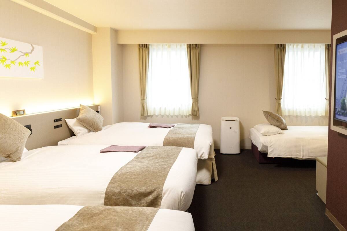 Ein Hotelzimmer mit zwei Betten, einem Wandfernseher und einem Fenster mit Vorhängen.