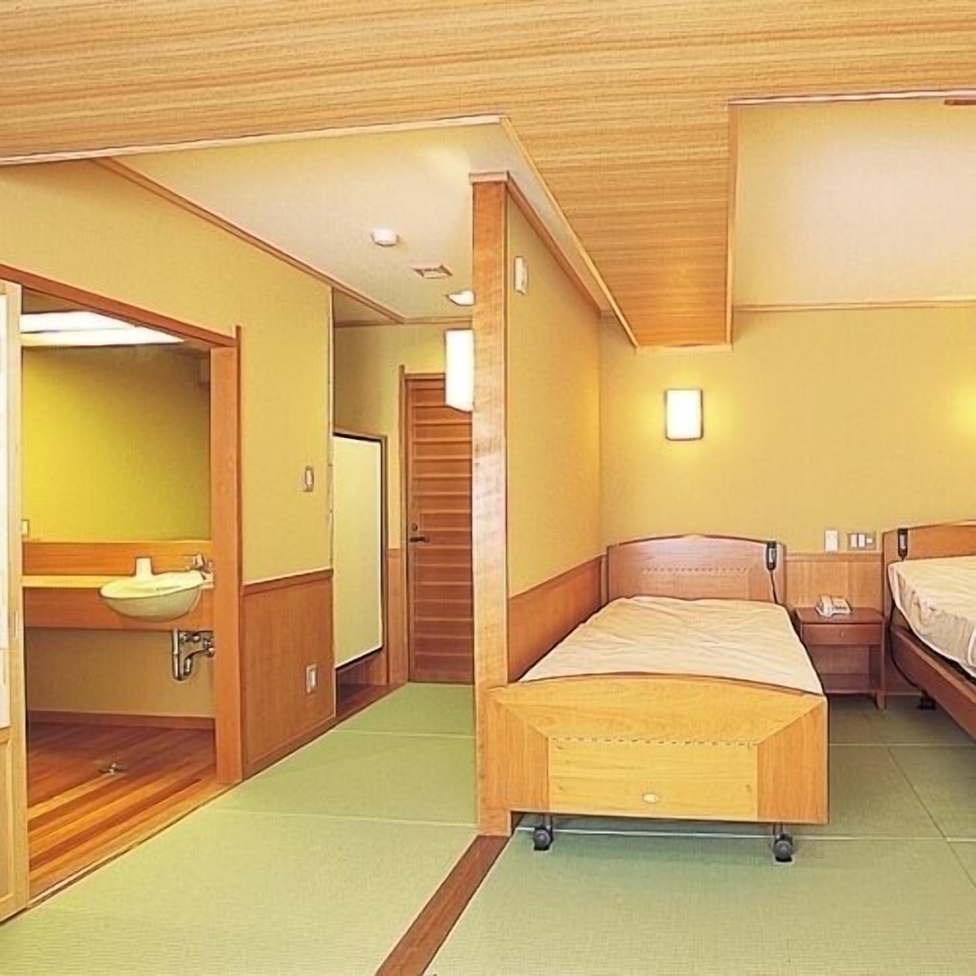 Habitación de hotel con cama de madera, una mesita de noche pequeña, un lavamanos integrado y un espejo.