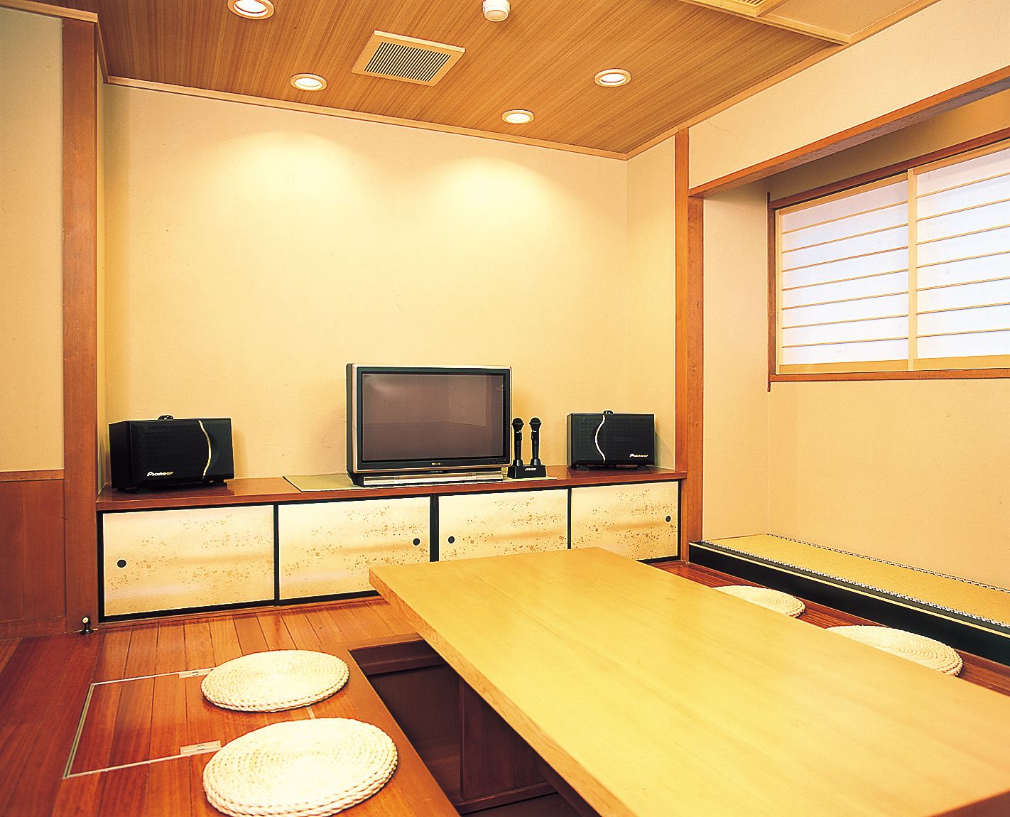 Una habitación con una mesa de madera, una televisión y altavoces sobre un mueble.
