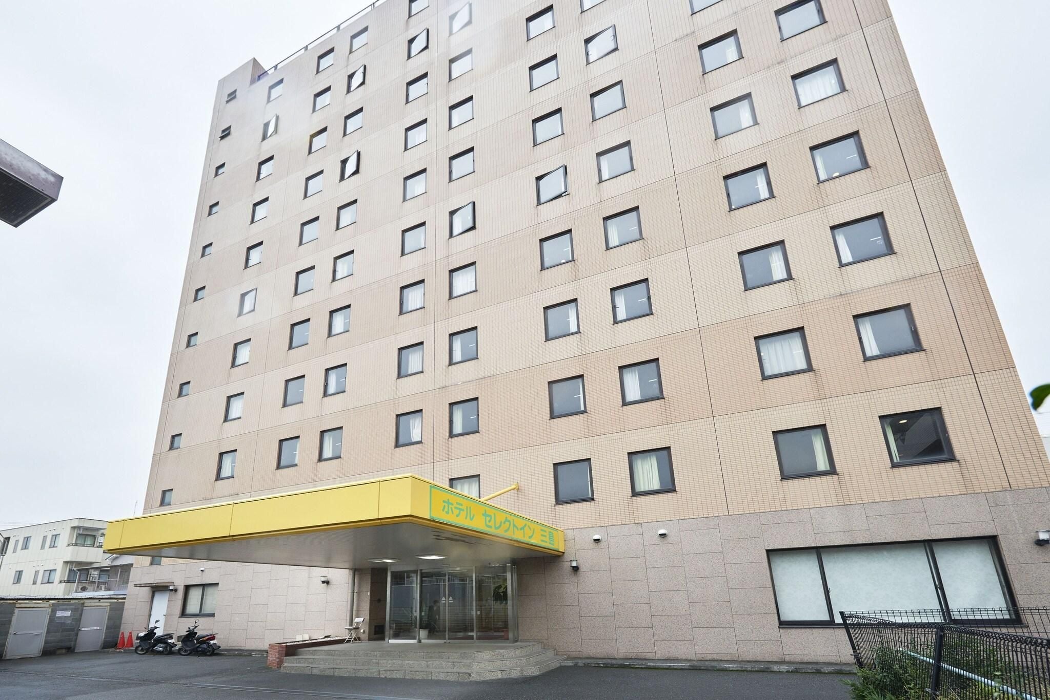 A multi-story hotel with a yellow entrance canopy, a parking area with motorcycles, and a large window on the right side.