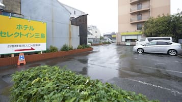 A hotel with a large signboard, a parking lot, and a building in the background.