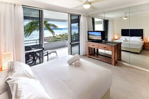 A hotel room with a large bed, a TV, a desk, and a balcony with a view of the ocean. - Frangipani 104 (Whitsundays)