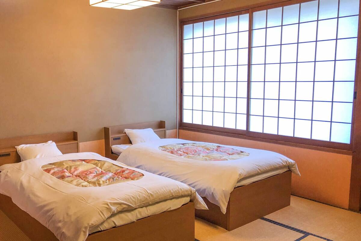 Two single beds with wooden headboards, a large window with grid panes, and a tatami mat floor.