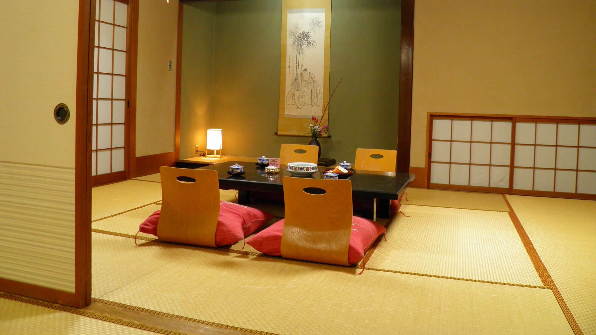 Une pièce de style japonais traditionnel, avec un sol recouvert de tatamis, une table basse avec des coussins et des portes coulissantes.