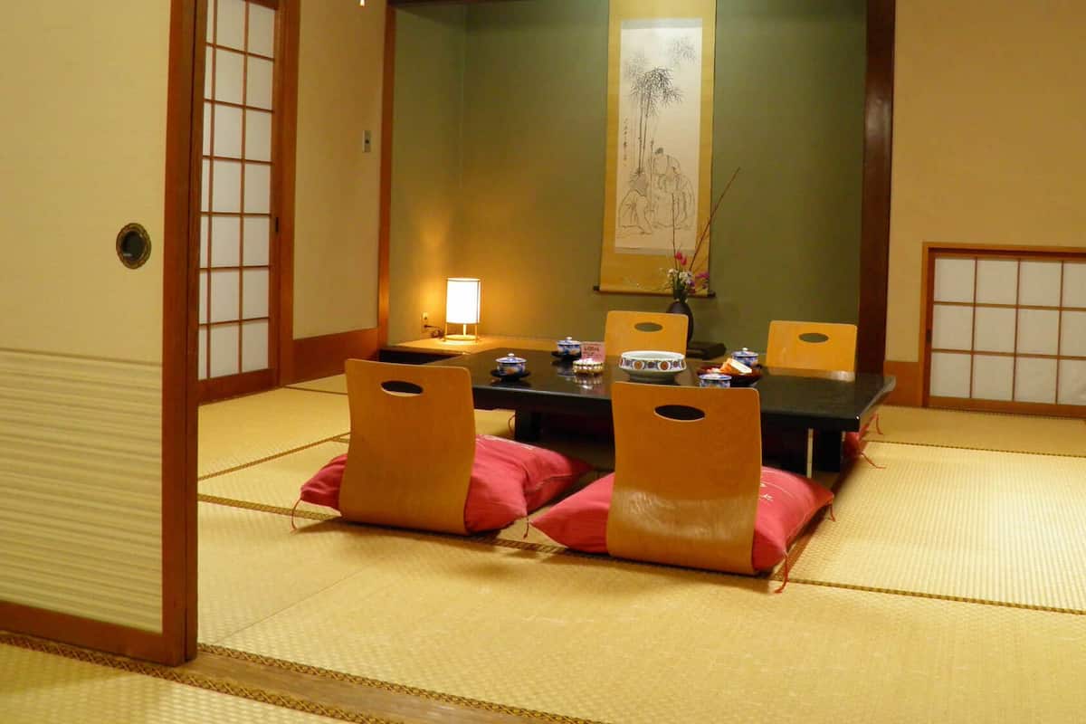 Une pièce de style japonais traditionnel, avec un sol recouvert de tatamis, une table basse avec des coussins et des portes coulissantes.