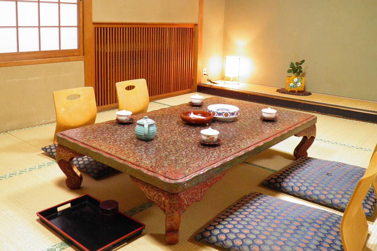 A traditional Japanese tatami room with a low table, cushions, and tea ceremony utensils.