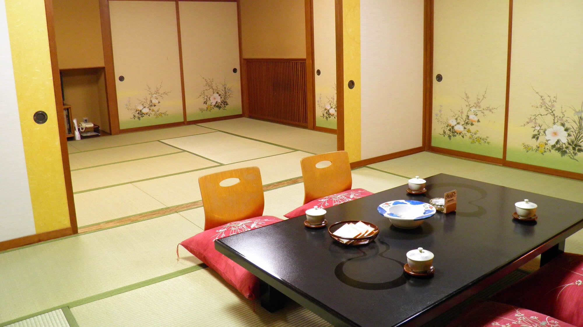 Perinteinen japanilainen huone, jossa on tatamimatto, matala pöytä teekupit ja -astiastot valmiina, sekä liukuovet, joissa on kukka-aiheisia kuvioita.