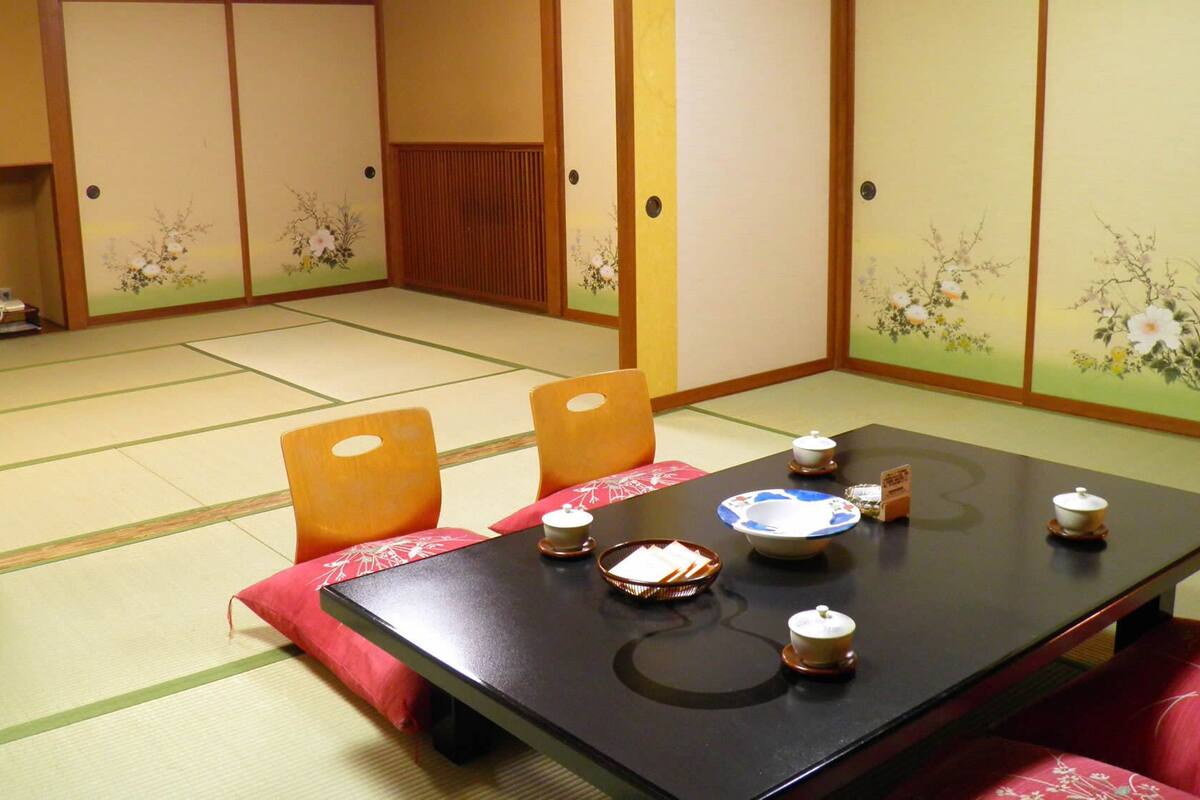 A traditional Japanese room with tatami flooring, a low table with a tea set, and sliding doors with floral designs.