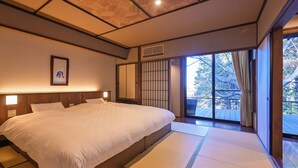 Un dormitorio de estilo japonés tradicional con una cama grande, cabecera de madera y puertas correderas que dan a un balcón.