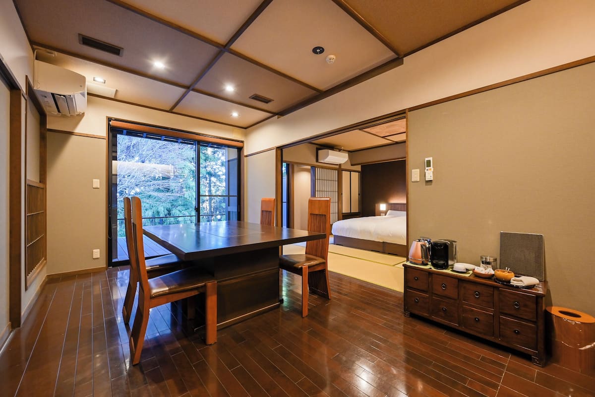 Habitación de hotel con una mesa de comedor de madera, sillas, una cama, un aparador y vistas al exterior.
