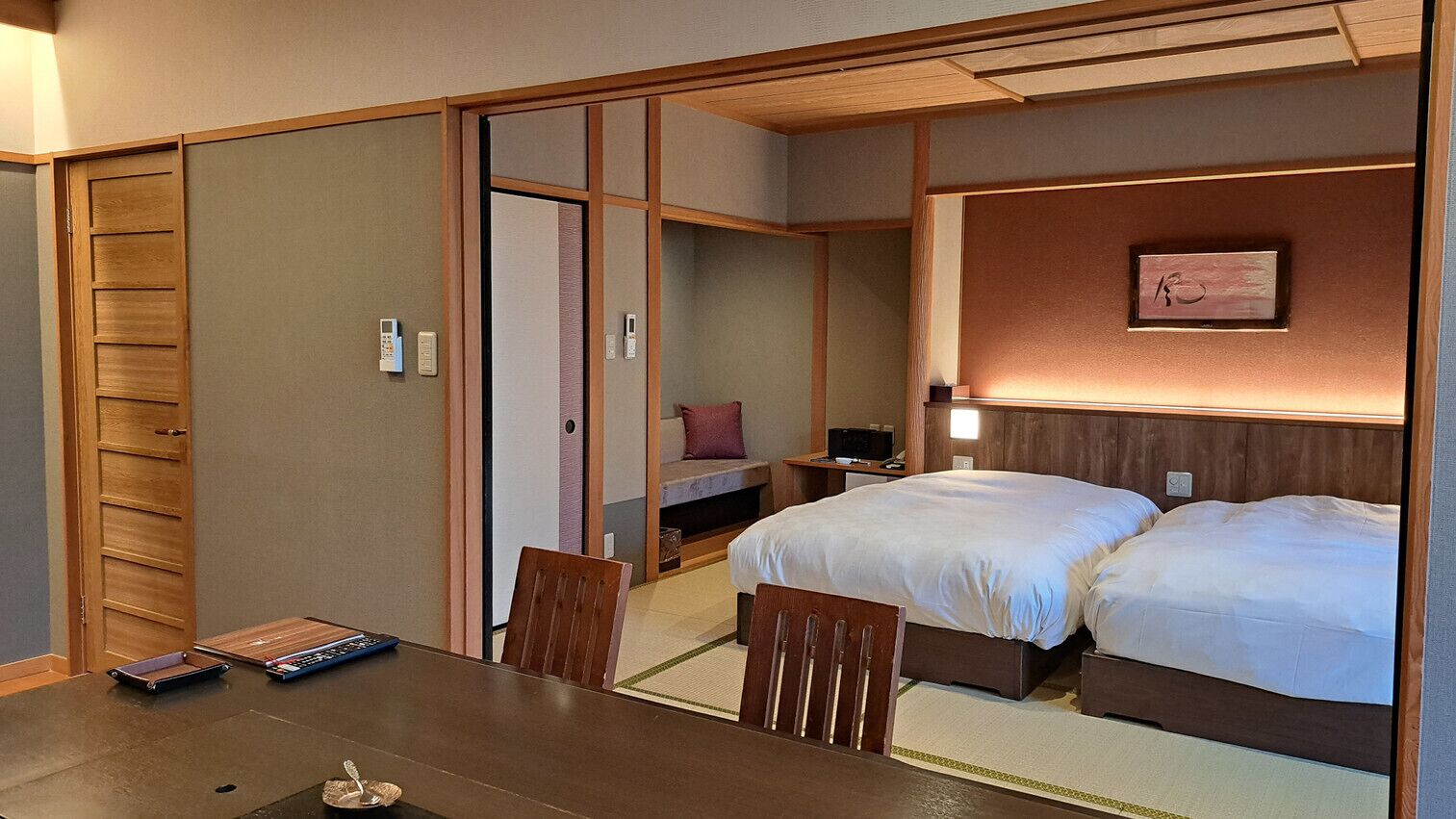 Una habitación tradicional japonesa con suelo de tatami, una cama de madera baja, un escritorio con silla y una puerta corrediza de shoji.