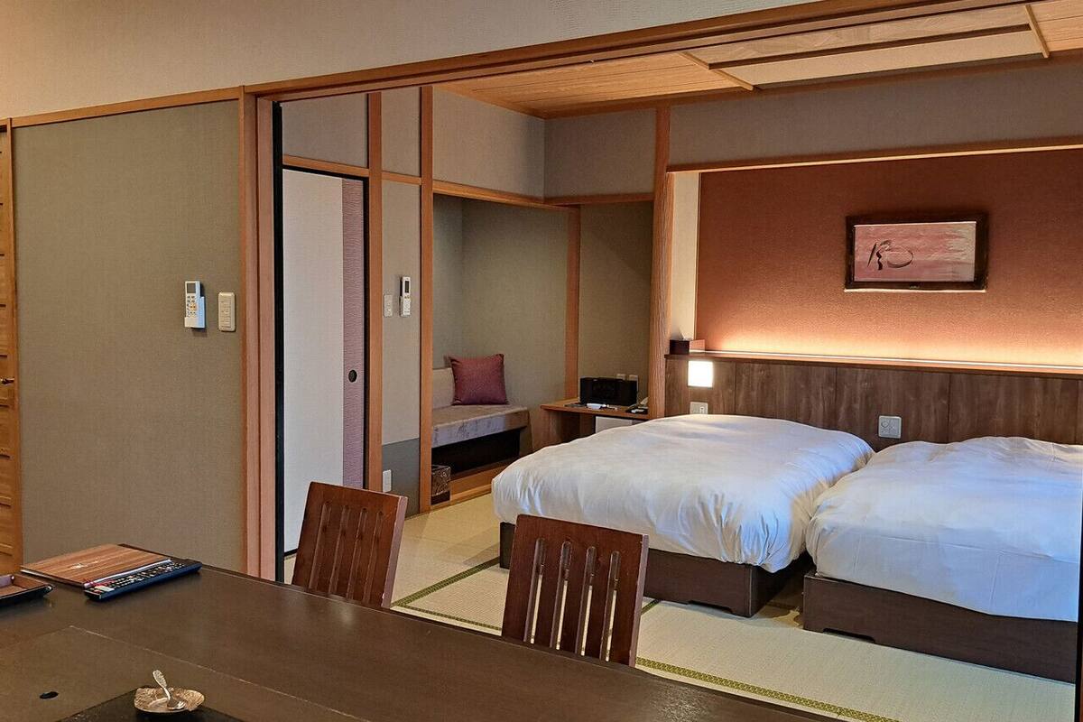 Una habitación tradicional japonesa con suelo de tatami, una cama de madera baja, un escritorio con silla y una puerta corrediza de shoji.