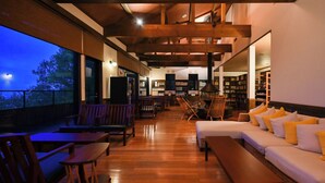 Amplio espacio interior con suelo de madera, un sofá con cojines amarillos, sillas de madera y una estantería.