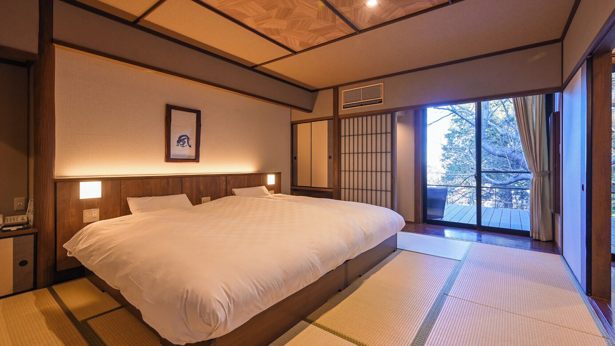 A traditional Japanese-style bedroom with tatami flooring, a large bed, sliding doors, and a view of the outdoors.