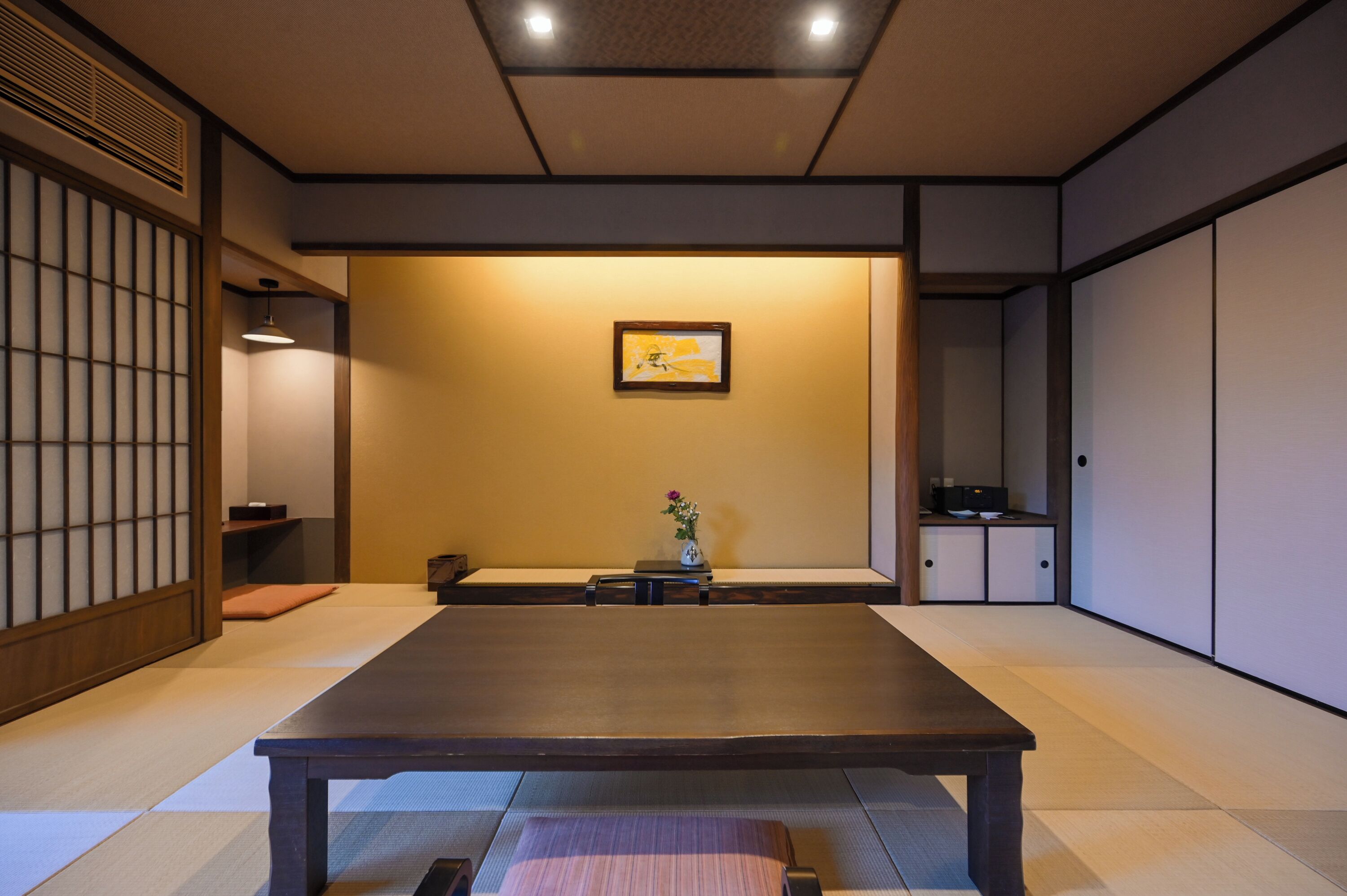 Una habitación tradicional japonesa con suelo de tatami, una mesa baja, puertas correderas y un cuadro en la pared.