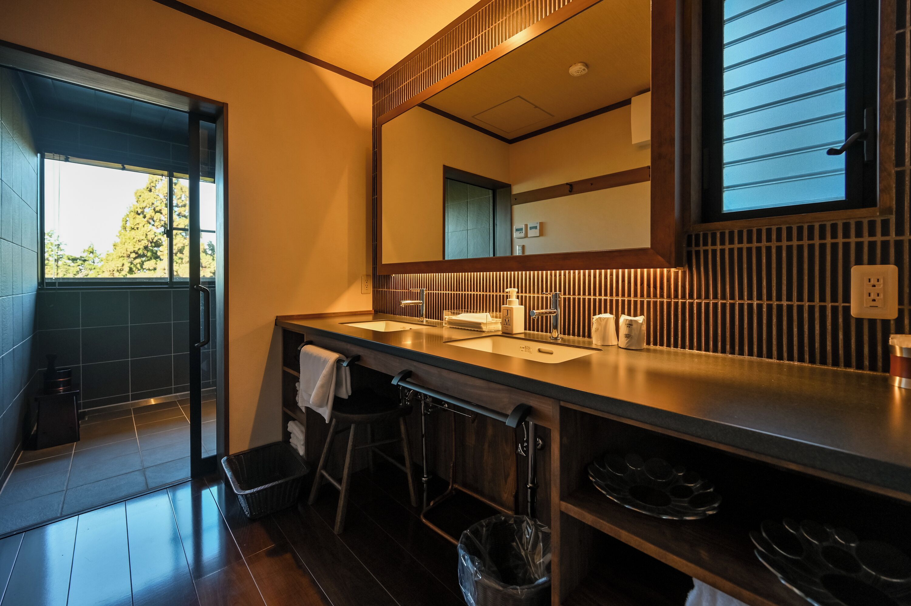 A modern bathroom with a large mirror, two sinks, and a window.