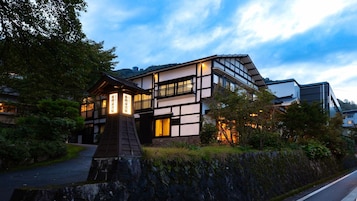 Un edificio japonés tradicional con una extensión moderna, que presenta un sendero de piedra y abundante vegetación.