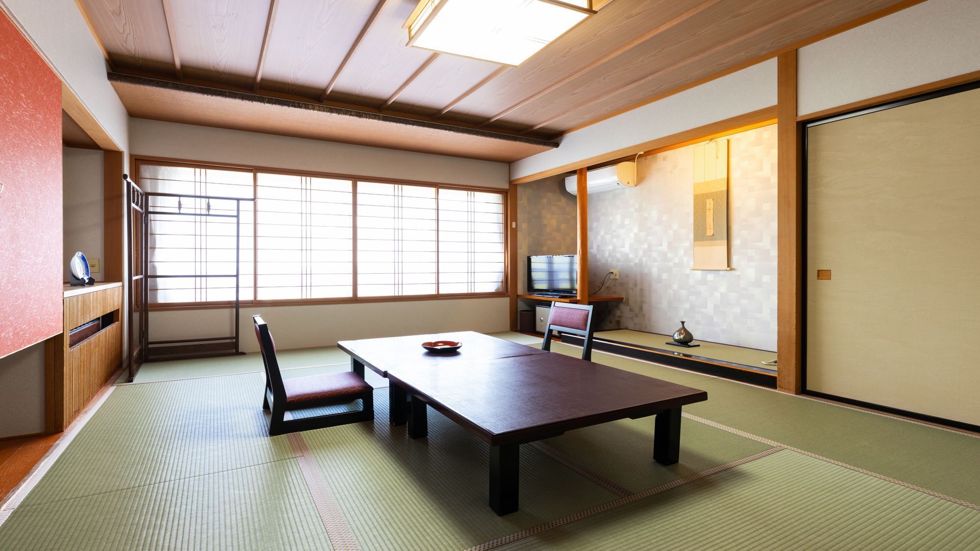 Ein traditioneller japanischer Raum mit Tatami-Bodenbelag, einem niedrigen Tisch, einem Sessel, einem Fernseher und Schiebetüren.