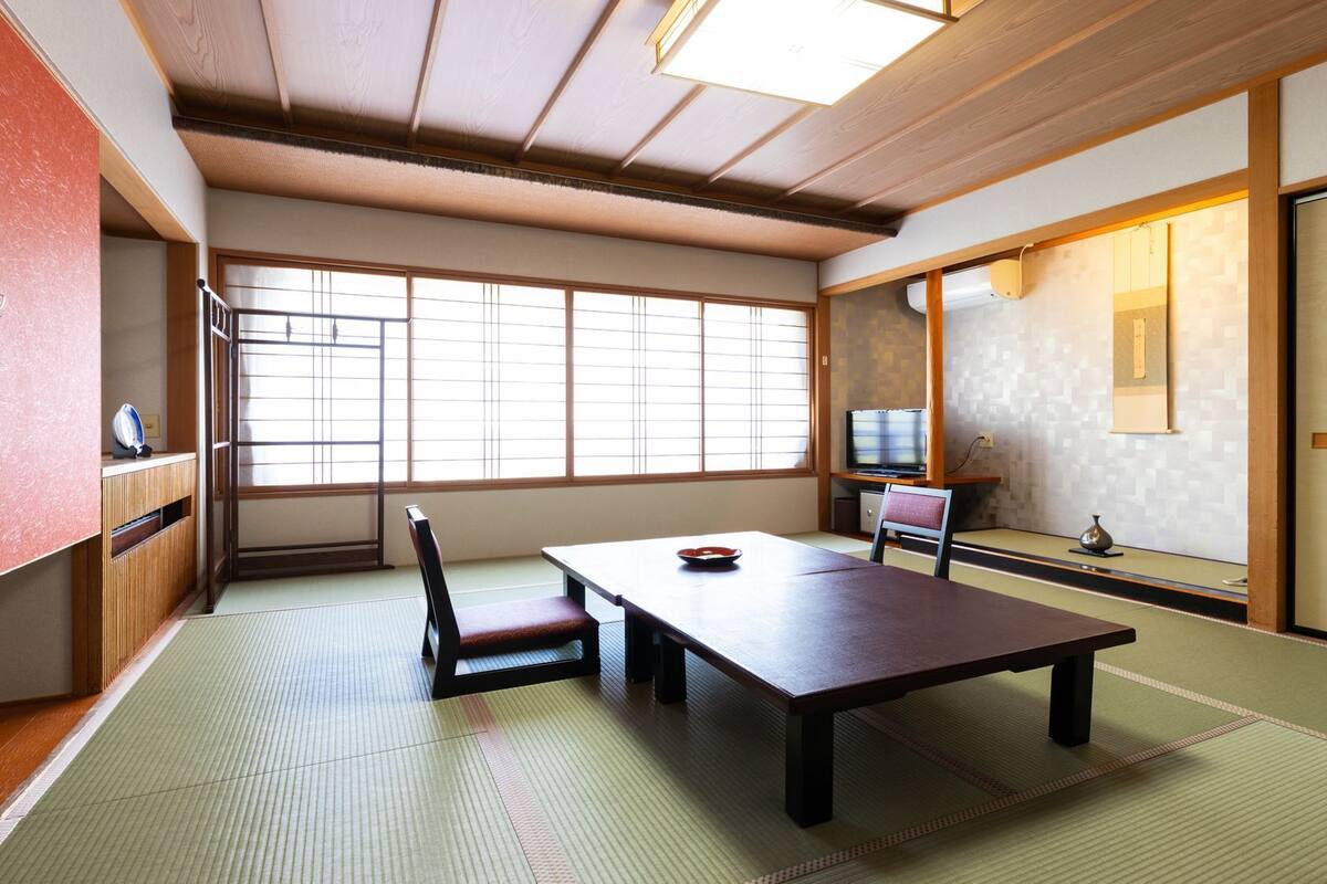 Ein traditioneller japanischer Raum mit Tatami-Bodenbelag, einem niedrigen Tisch, einem Sessel, einem Fernseher und Schiebetüren.
