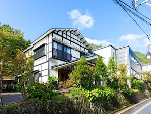 A modern two-story building with a balcony, surrounded by greenery and a stone wall. - Otowaya Ryokan (Yuzawa)