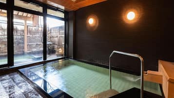 A hot tub with a wooden floor, a metal railing, and a view of a snowy outdoor area through large windows.