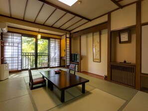 A traditional Japanese room with tatami flooring, a low table, a television, and sliding doors. - Otowaya Ryokan (Yuzawa)