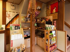 A traditional Japanese store with wooden shelves stocked with various goods, a fan, and a framed painting. - Otowaya Ryokan (Yuzawa)