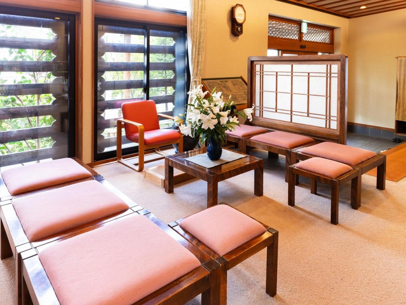 A room with wooden furniture, including a sofa and chairs, a table with a vase of flowers, and a traditional Japanese sliding door.
