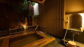 A traditional Japanese onsen with a wooden bench, a small wooden stool, and a stone bath.