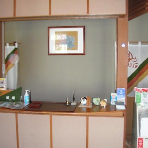 A reception desk with a framed picture above it, a small clock, and various items on the counter including a bottle and a fan. - Otowaya Ryokan (Yuzawa)