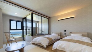 Una habitación de hotel moderna con dos camas, un balcón con vistas al mar, una mesita y una silla.