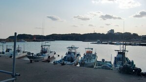 Un puerto con barcos amarrados, un faro y una colina con una construcción al fondo.